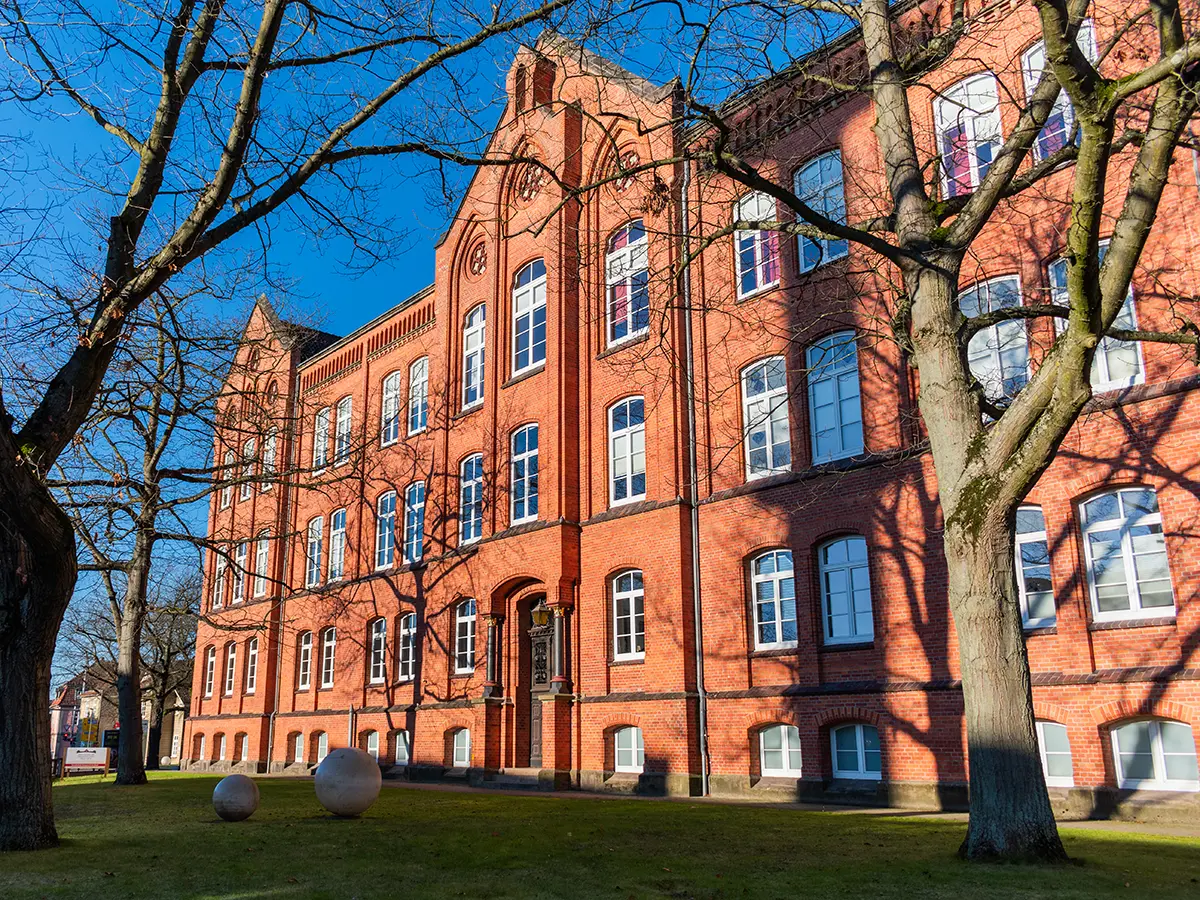 Historisches Backsteingebäude in Celle, Standort der Physiotherapie-Praxis PhysioTeam Riemke, umgeben von Bäumen und Grünflächen.