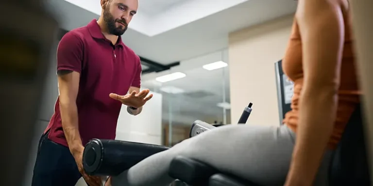 Physiotherapeut begleitet Patientin bei einer Übung am Trainingsgerät zur Kräftigung der Beinmuskulatur in der Krankengymnastik.