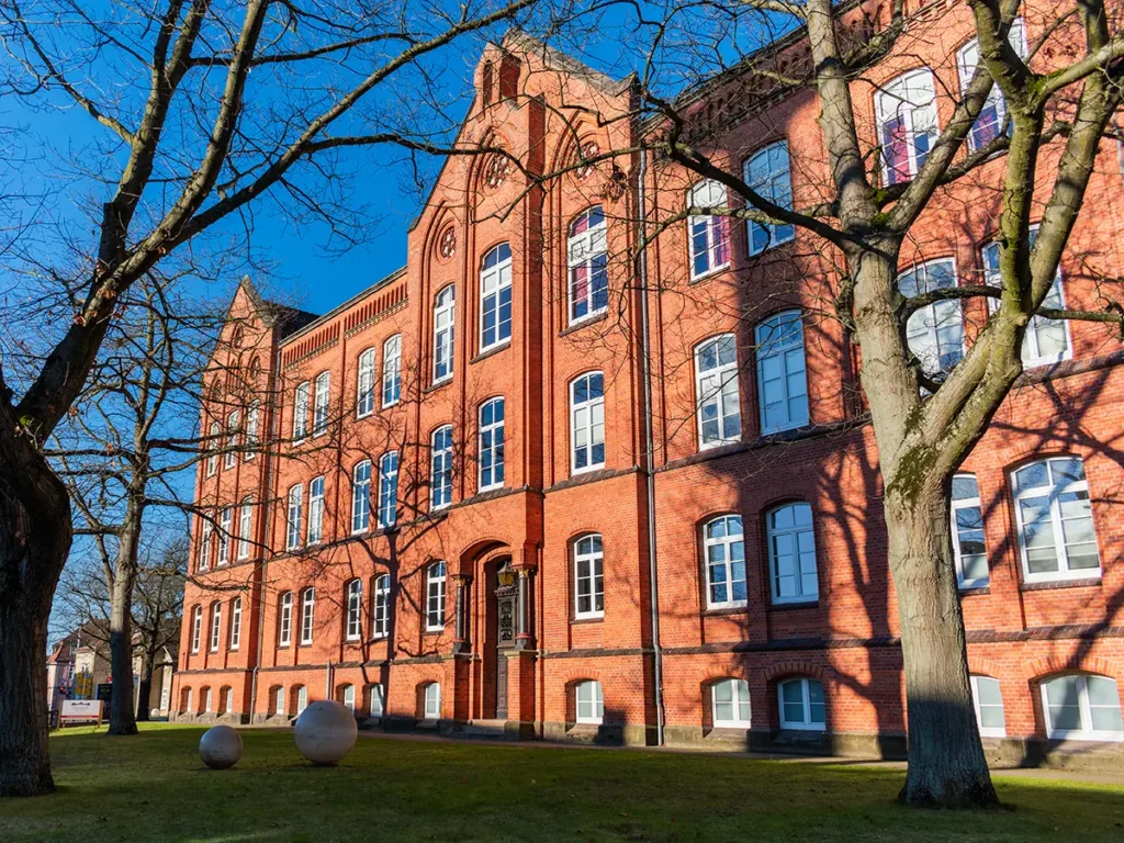 Historisches Backsteingebäude in Celle, Standort der Physiotherapie-Praxis PhysioTeam Riemke, umgeben von Bäumen und Grünflächen.