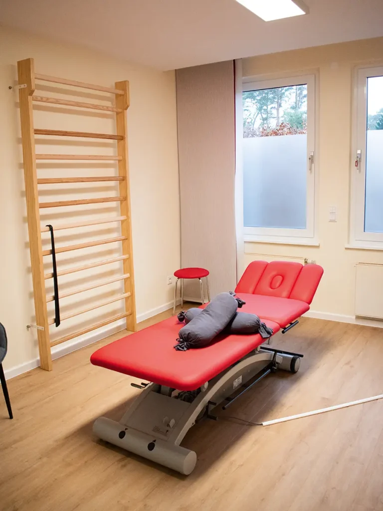 Behandlungsraum in der Physiotherapie Mobili Klein Hehlen mit roter Liege, Sprossenwand und großen Fenstern.