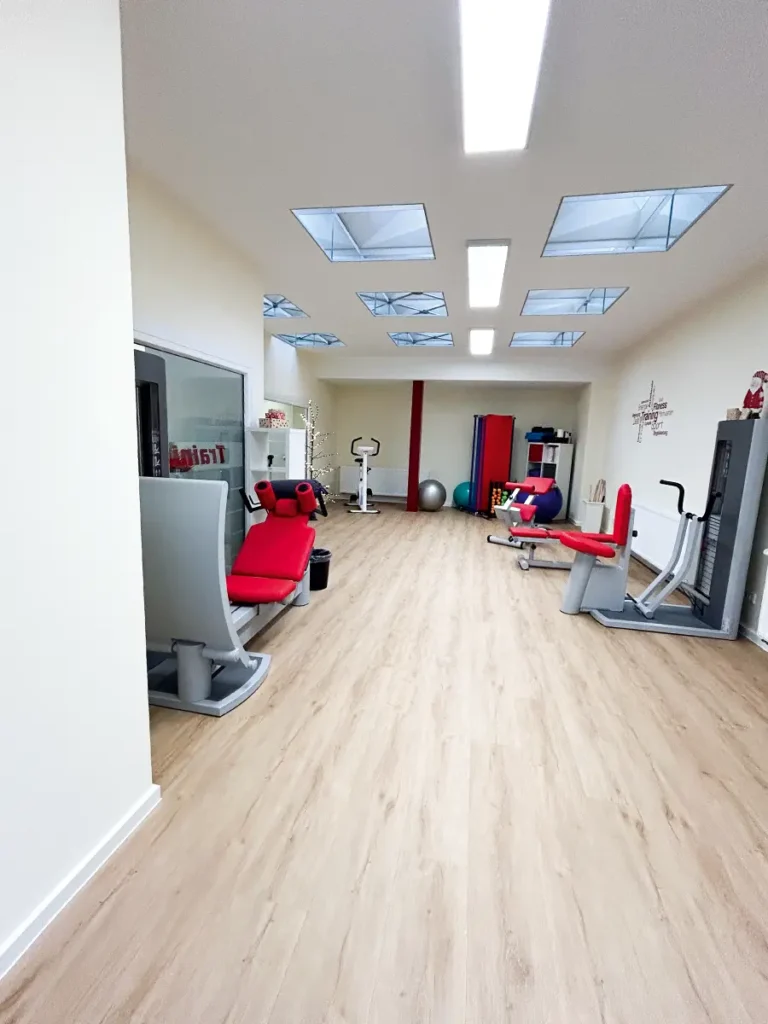 Trainingsraum der Physiotherapie Mobili Klein Hehlen mit modernen Geräten, roten Sitzpolstern und hellem Holzfußboden.