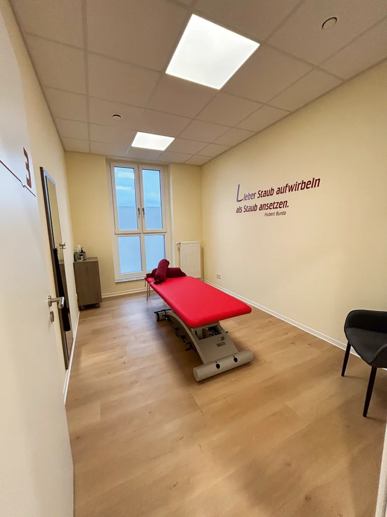 Behandlungsraum der Physiotherapie Mobili Misburg mit roter Therapieliege und motivierendem Wandzitat.