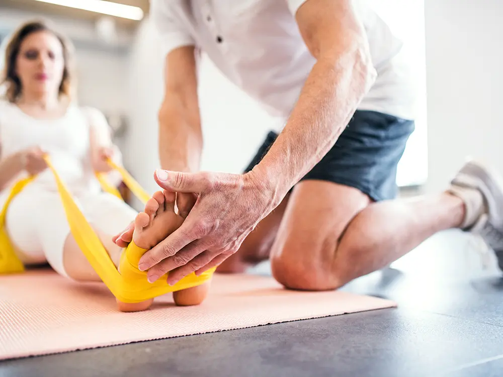 Physiotherapeut führt mit einer Patientin Übungen mit einem gelben Theraband durch, Fokus auf Mobilisation und Rehabilitation.