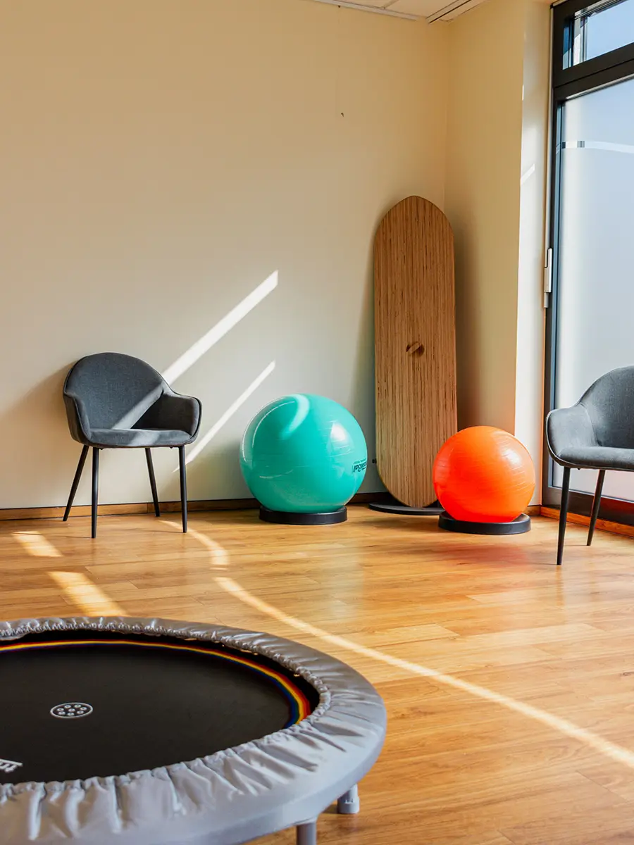 Ergotherapieraum mit Gymnastikbällen, Trampolin und Therapiegeräten in heller, freundlicher Umgebung.