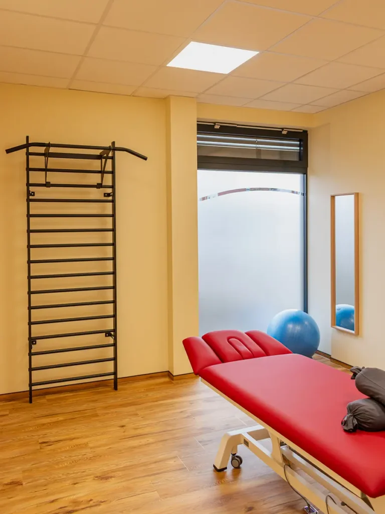 Moderner Behandlungsraum mit Therapieliege, Sprossenwand und Gymnastikball für Physiotherapie.